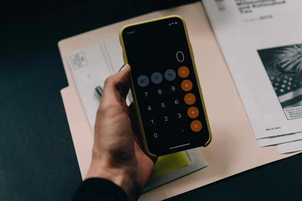 mão de homem trabalhando com calculadora no celular e papeis para realizar o fluxo de caixa operacional da empresa